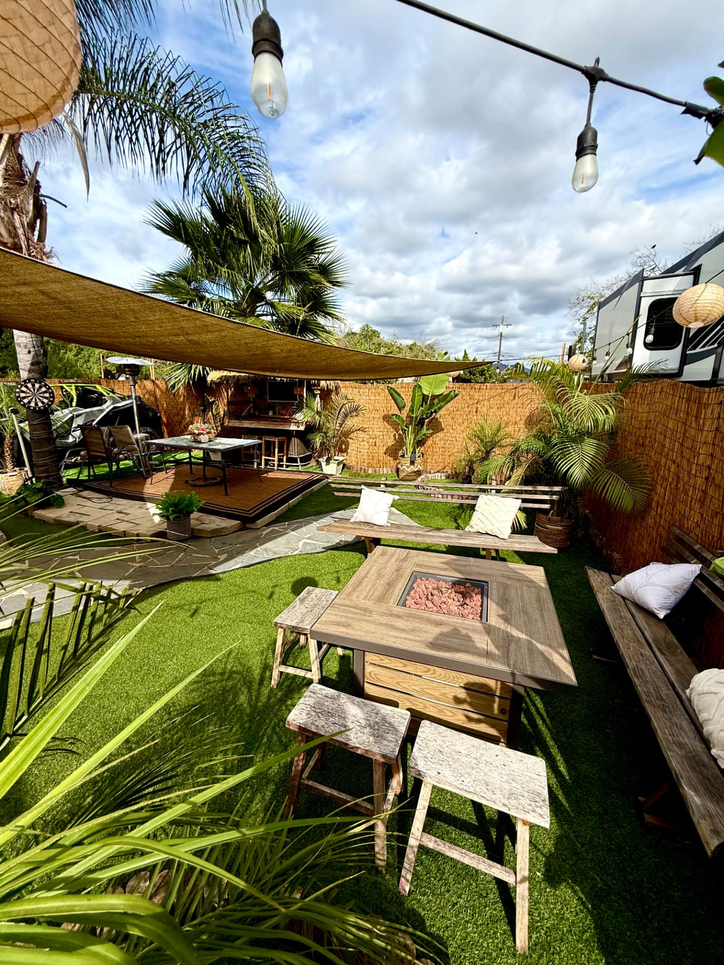 Wide view of Casa Tulum's tropical backyard with fire pit, shade sails and palms